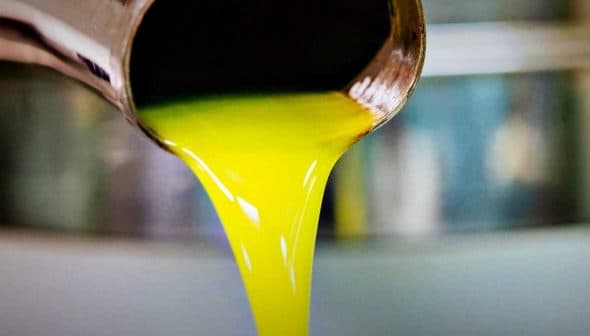 Golden olive oil pouring from a metal spout into a container. - Olive Oil Times