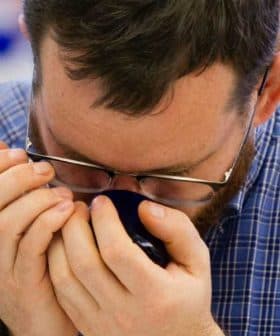 Individual with glasses holding a coffee cup close to their face, inhaling the aroma. - Olive Oil Times