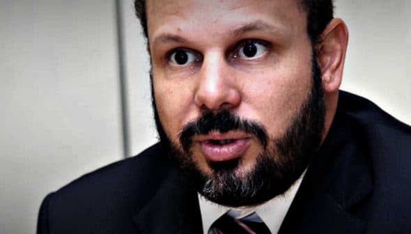 Man with a beard wearing a suit and tie, speaking during a meeting or interview. - Olive Oil Times