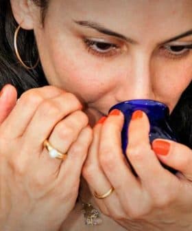 Woman with dark hair holding a blue cup close to her face, preparing to smell its contents. - Olive Oil Times