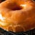 A close-up of a glazed doughnut resting on a wire cooling rack. - Olive Oil Times