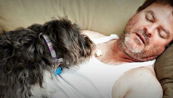 A man sleeping on a couch with a small dog resting beside him. - Olive Oil Times