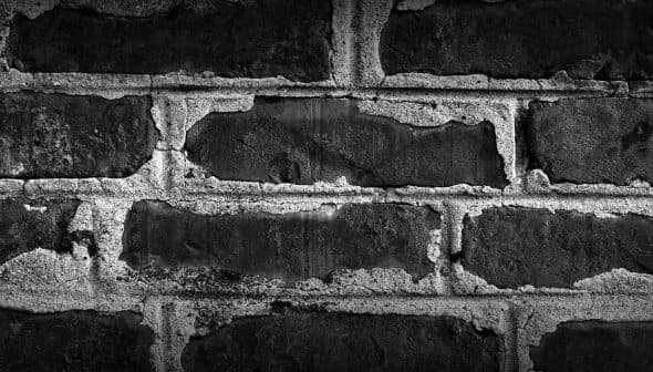 Close-up view of a textured black and white brick wall with visible mortar and wear. - Olive Oil Times