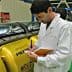 Man in a lab coat taking notes while observing yellow machinery in a facility. - Olive Oil Times