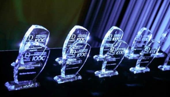 Row of crystal awards with engraved text on a dark surface illuminated by blue light. - Olive Oil Times