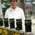 Row of olive oil bottles on a production line with a worker in the background. - Olive Oil Times