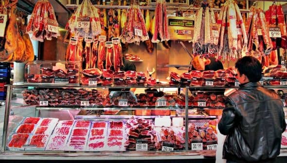 A variety of meats displayed in a market stall with price tags visible. - Olive Oil Times