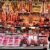 A variety of meats displayed in a market stall with price tags visible. - Olive Oil Times