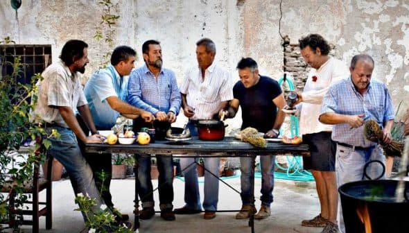 A group of men gathered around a table preparing food outdoors in a rustic setting. - Olive Oil Times