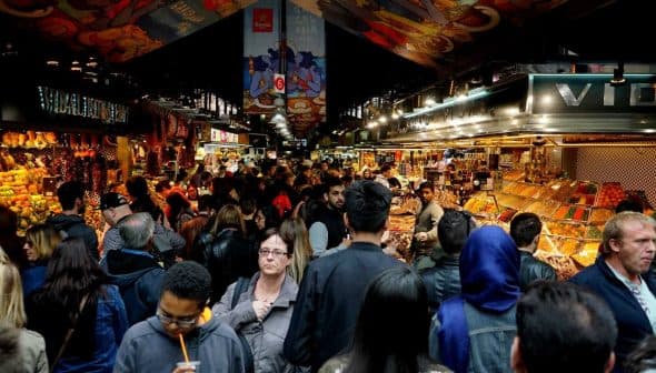 A busy marketplace filled with people browsing various stalls and displays of goods. - Olive Oil Times