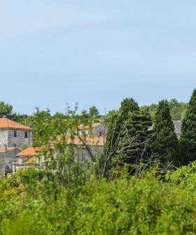 A village landscape featuring a church tower and traditional buildings among greenery. - Olive Oil Times