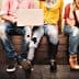 A group of young individuals sitting side by side, engaged with various devices and wearing casual clothing. - Olive Oil Times