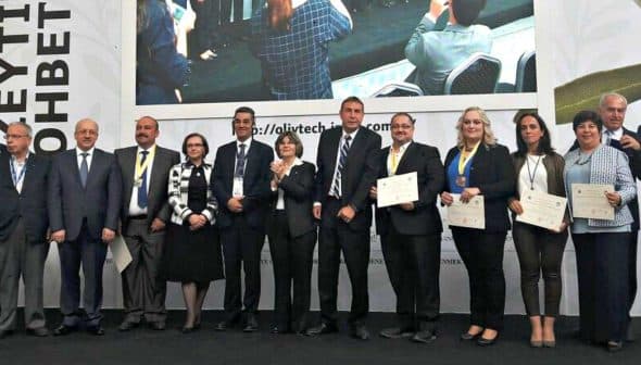 A group of individuals standing together on stage holding certificates at an event. - Olive Oil Times