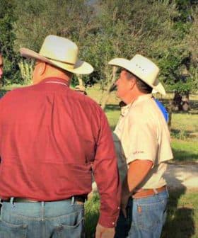 A group of individuals wearing hats engaged in conversation outdoors in a natural setting. - Olive Oil Times