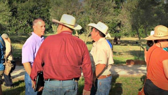 A group of individuals wearing hats engaged in conversation outdoors in a natural setting. - Olive Oil Times