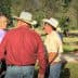 A group of individuals wearing hats engaged in conversation outdoors in a natural setting. - Olive Oil Times