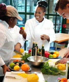 Three chefs in a culinary class preparing ingredients with fruits and vegetables on a table. - Olive Oil Times