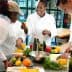 Three chefs in a culinary class preparing ingredients with fruits and vegetables on a table. - Olive Oil Times