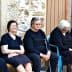 Six elderly women dressed in black and one in pink sitting on a bench outside a building. - Olive Oil Times