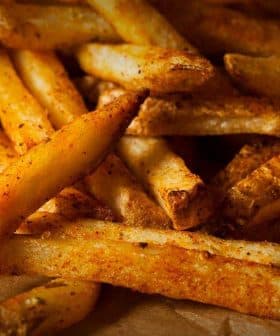 A pile of golden brown French fries seasoned with spices on a piece of parchment paper. - Olive Oil Times