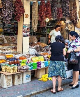 A market scene featuring various spices and dried goods displayed on tables with shoppers interacting. - Olive Oil Times