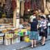 A market scene featuring various spices and dried goods displayed on tables with shoppers interacting. - Olive Oil Times