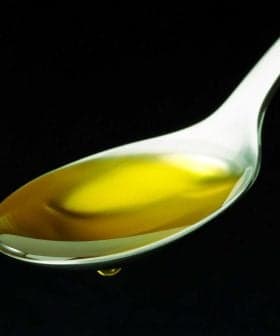 A spoon filled with golden olive oil against a black background.