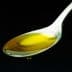 A spoon filled with golden olive oil against a black background.