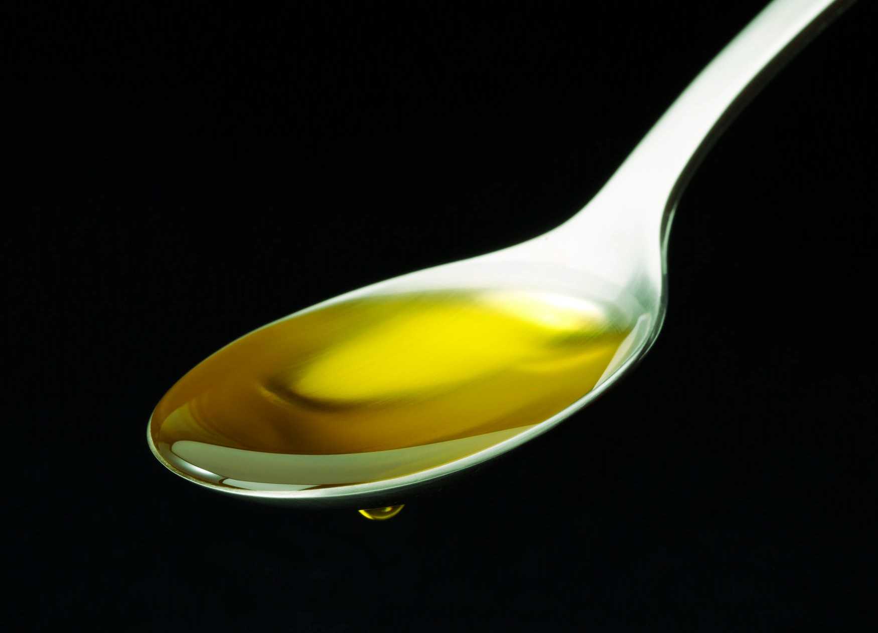 A spoon filled with golden olive oil against a black background.