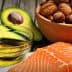 Raw salmon fillet placed on a white surface with a bowl of nuts and sliced avocado in the background. - Olive Oil Times