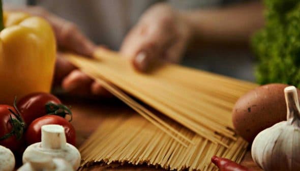 Raw spaghetti, tomatoes, garlic, mushrooms, yellow bell pepper, and eggs arranged on a wooden surface. - Olive Oil Times