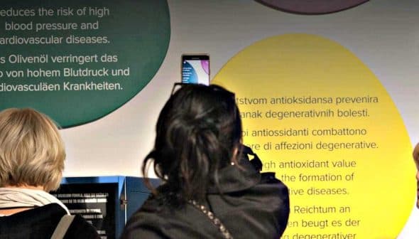Two women viewing informational displays about health benefits of olive oil at an exhibit. - Olive Oil Times