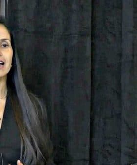 A woman with long hair speaking at a podium during a presentation at a conference. - Olive Oil Times