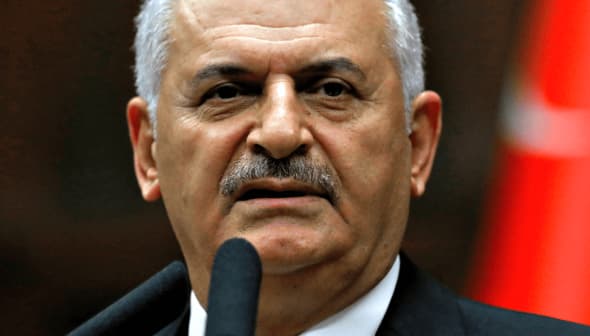 A Turkish politician speaking at a podium with a microphone, Turkish flag in the background. - Olive Oil Times