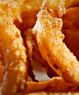 Close-up of crispy fried onion rings arranged in a circular pattern. - Olive Oil Times