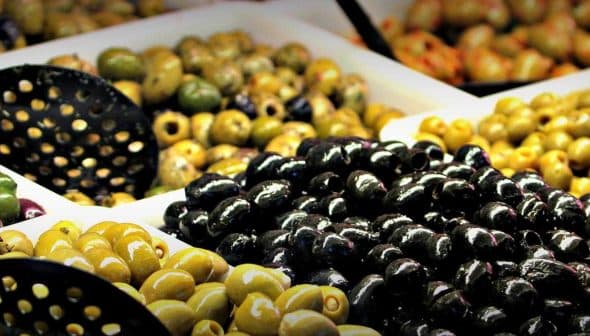 Assorted olives in various colors and sizes displayed in baskets with serving utensils. - Olive Oil Times