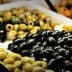 Assorted olives in various colors and sizes displayed in baskets with serving utensils. - Olive Oil Times