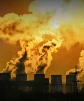 Smoke billowing from multiple smokestacks of an industrial power plant against a sunset backdrop. - Olive Oil Times