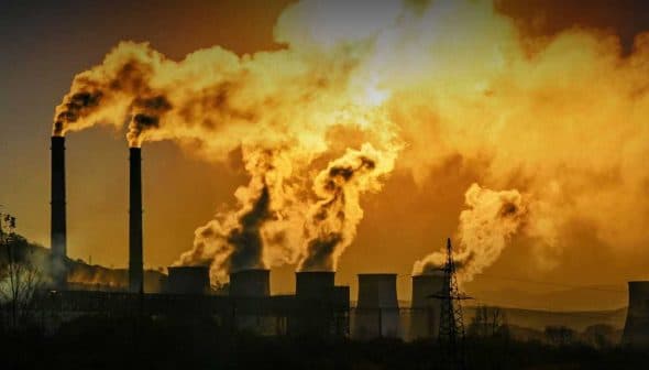 Smoke billowing from multiple smokestacks of an industrial power plant against a sunset backdrop. - Olive Oil Times