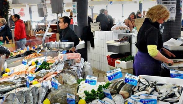 A seafood market featuring various types of fresh fish and seafood on display at vendor stalls. - Olive Oil Times