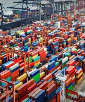 Aerial view of a busy port with numerous shipping containers and a cargo ship docked. - Olive Oil Times