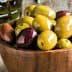 A wooden bowl filled with various types of olives including green and black varieties. - Olive Oil Times