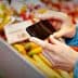 Individual holding a smartphone while photographing colorful vegetables at a market stall. - Olive Oil Times