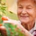 Elderly woman wearing a straw hat picking tomatoes from a plant in a garden. - Olive Oil Times