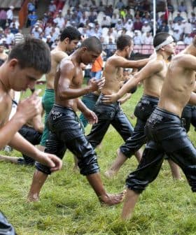 Young men in wet clothing walking in a line during a traditional event on a grassy field. - Olive Oil Times