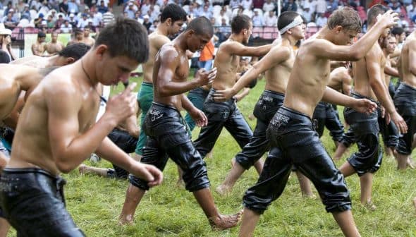 Young men in wet clothing walking in a line during a traditional event on a grassy field. - Olive Oil Times