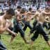 Young men in wet clothing walking in a line during a traditional event on a grassy field. - Olive Oil Times