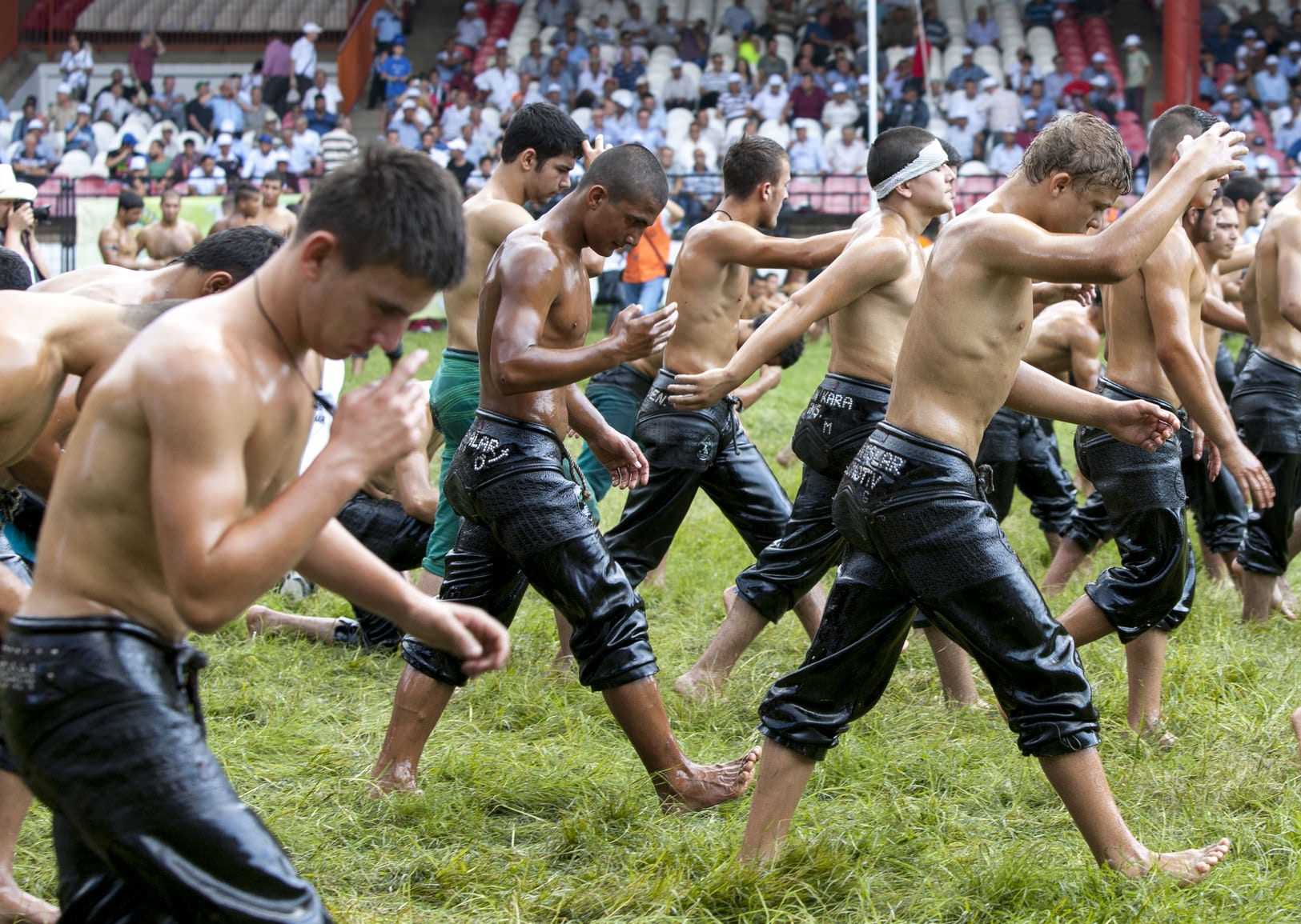 Young men in wet clothing walking in a line during a traditional event on a grassy field. - Olive Oil Times