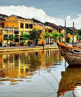 Traditional wooden boats moored on a river with reflections of buildings in Hoi An, Vietnam. - Olive Oil Times