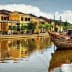 Traditional wooden boats moored on a river with reflections of buildings in Hoi An, Vietnam. - Olive Oil Times
